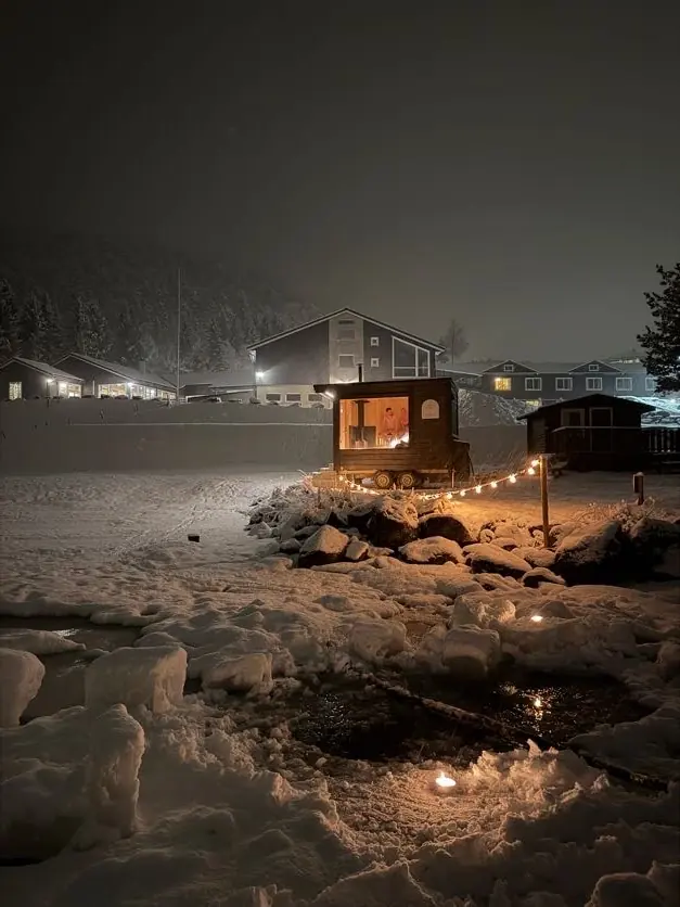 Badstue på tilhenger med lys i snøen om kvelden